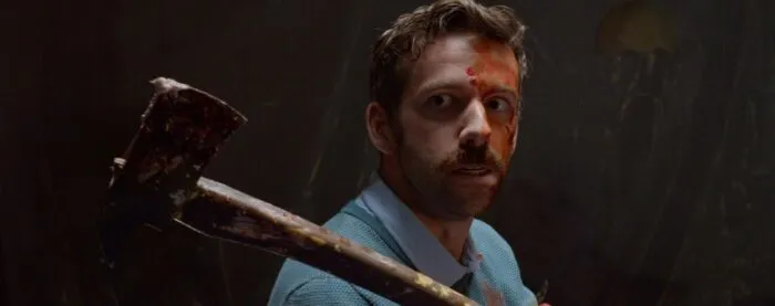 A man with blood on his brow carries an axe on his shoulder.
