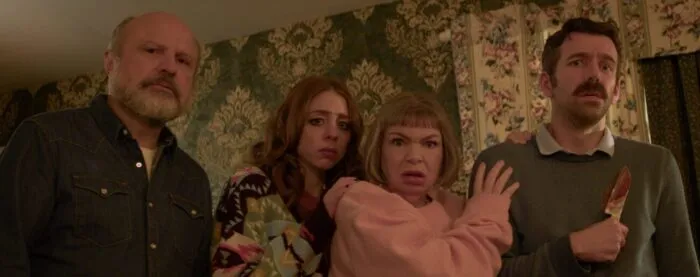 Four people standing next to each other in a house with green and gold wallpaper.