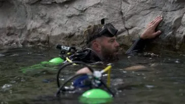 In the waters of Calamity Lake, Chad Ollinger holds onto the limestone rock wall to rest (camera person Ryan Powers in foreground)