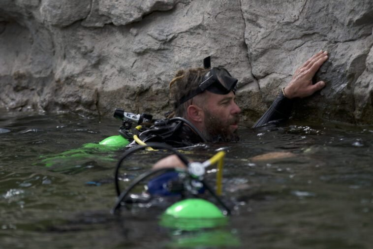 In the waters of Calamity Lake, Chad Ollinger holds onto the limestone rock wall to rest (camera person Ryan Powers in foreground)