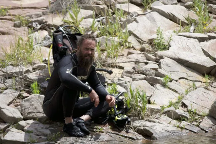 On the rocky shoreline of Calamity Lake, Chad Ollinger (in full SCUBA gear) prepares for his dive