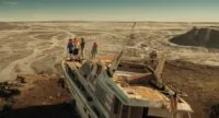 A group of people in life preservers stand on the bow of a boat in the middle of a desert.