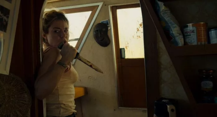A woman with a knife hides around a corner on a boat