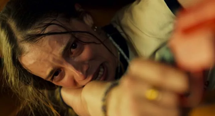 A conflicted woman holds an orange gun in SURVIVE