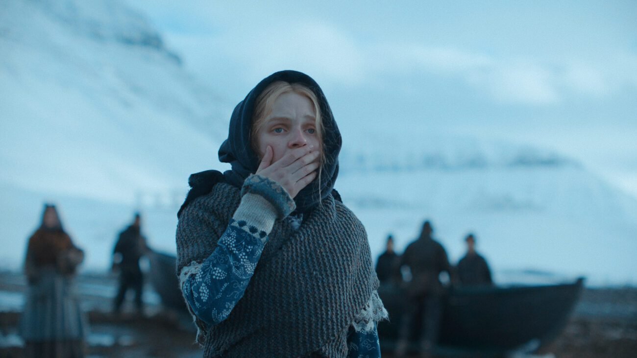 A woman holds her hand over her mouth in shock as men gather in the background.