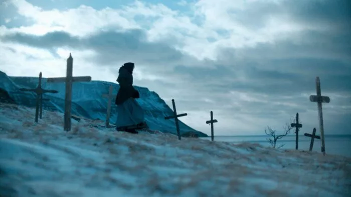 A woman walks down a snowy hillside through a field of crosses.