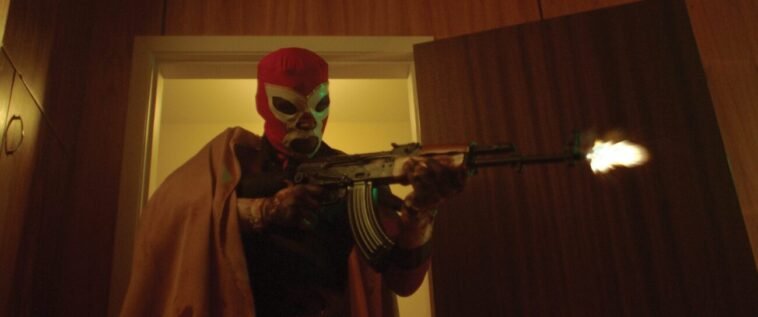 A man in a luchador mask holds a shotgun in a doorway in DARK MATCH