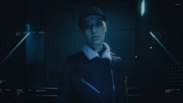 A woman in a buttoned up jacket and baseball cap is seen through a security camera