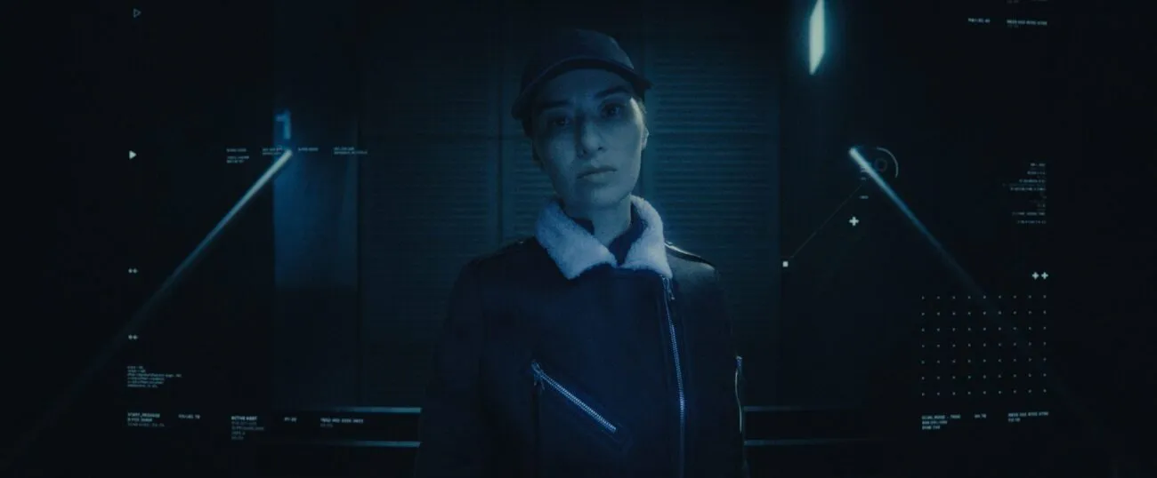 A woman in a buttoned up jacket and baseball cap is seen through a security camera