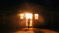 A person stands in the doorway of a burning house.