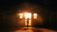 A person stands in the doorway of a burning house.
