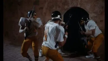 A group of football players hold guns while entering a doorway.