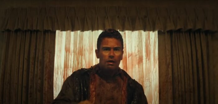 A man and the curtains behind him are covered in blood in THE MONKEY
