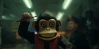 A toy monkey is shown with it's right arm raised under fluorescent lights. THE MONKEY