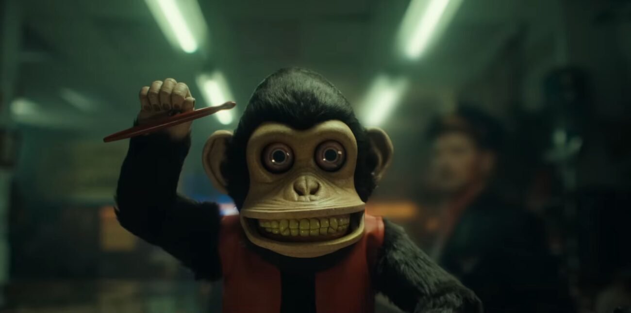 A toy monkey is shown with it's right arm raised under fluorescent lights. THE MONKEY