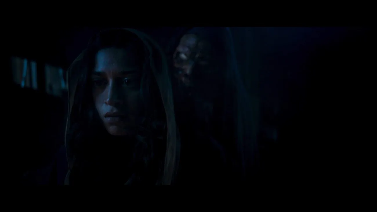 A demonic being lurks in the darkness behind a woman in Virgin.