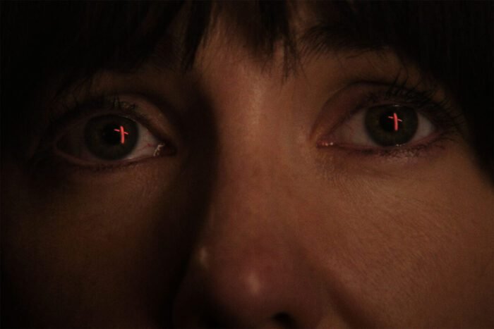 A close up shot on a woman's eyes where the fiery reflection of a cross burning resides