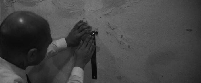 A man measures a hole in the wall with a ruler in HEAD LIKE A HOLE