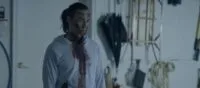 A man dressed in white is covered in blood while standing in a garage.