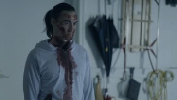 A man dressed in white is covered in blood while standing in a garage.