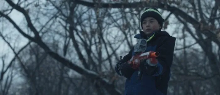A young boy in winter clothing holds a nerf gun in a winter scene of UNCONTAINED