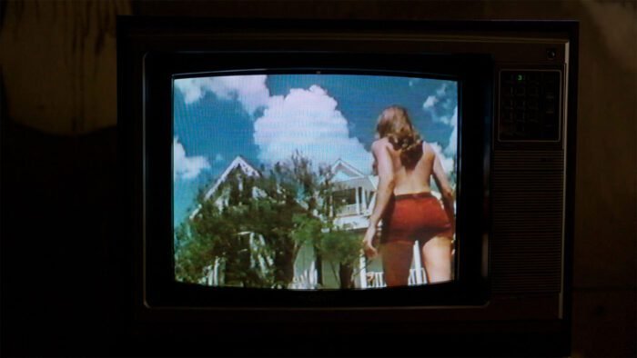 a tv showing a scene from THE TEXAS CHAINSAW MASSACRE of a woman walking toward a house under a vibrantly blue sky.