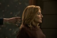 a hand reaches into the hair of a woman who is looking in the oppositte direction.