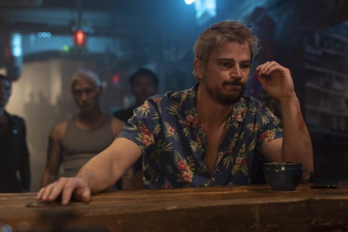 A haggard looking man sits at a bar while a group of men gathers behind him in Fight or Flight.
