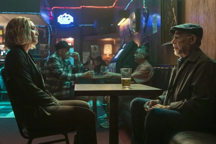 A woman sits opposite an older man at a table in a bar.