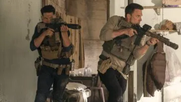 two men holding powerful riffles and wearing body armor emerge from a doorway in THE ACCOUNTANT 2