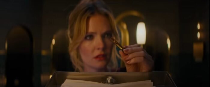 A woman looks at a vial of liquid over a card catalogue.