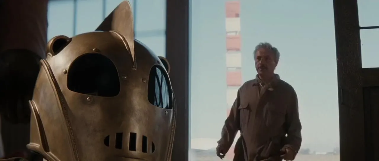 A older man walks into an airport hanger and looks at a bronze helmet sitting on a table