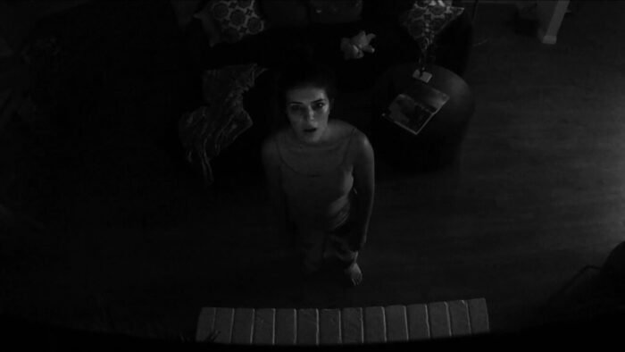 A woman stares into a black and white camera above her