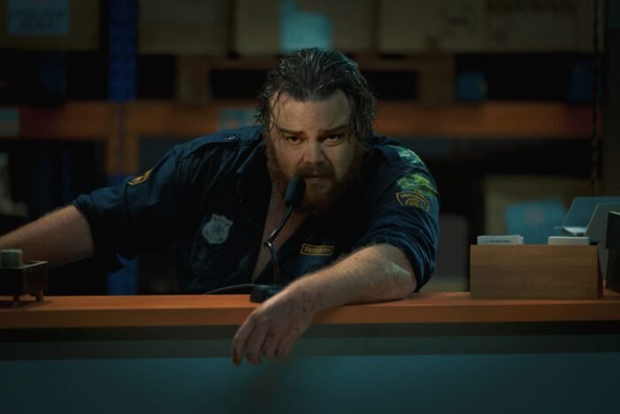 A burly man leans over a warehouse railing in WAKE UP