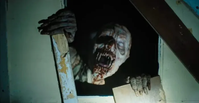 a monstrous zombie-looking face emerges from a square hole in a door where a glass pane once was located.