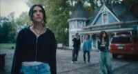 A woman pulls focus away from her group in the background standing outside of a blue house