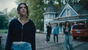 A woman pulls focus away from her group in the background standing outside of a blue house