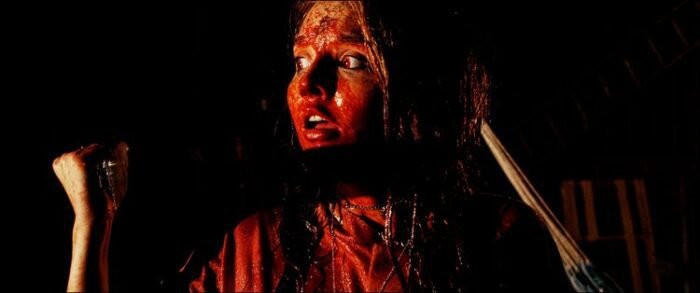 A woman covered in blood holds a knife