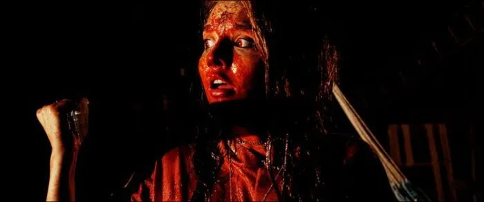 A woman covered in blood holds a knife