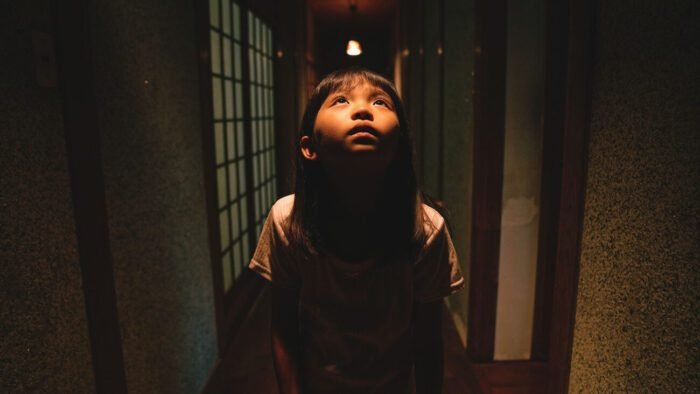 A young boy looks up into a light in a low lit hallway in BEST WISHES TO ALL