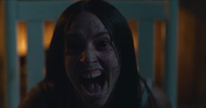 A woman with dark veigns and black eyes is seen laughing viciously in a chair