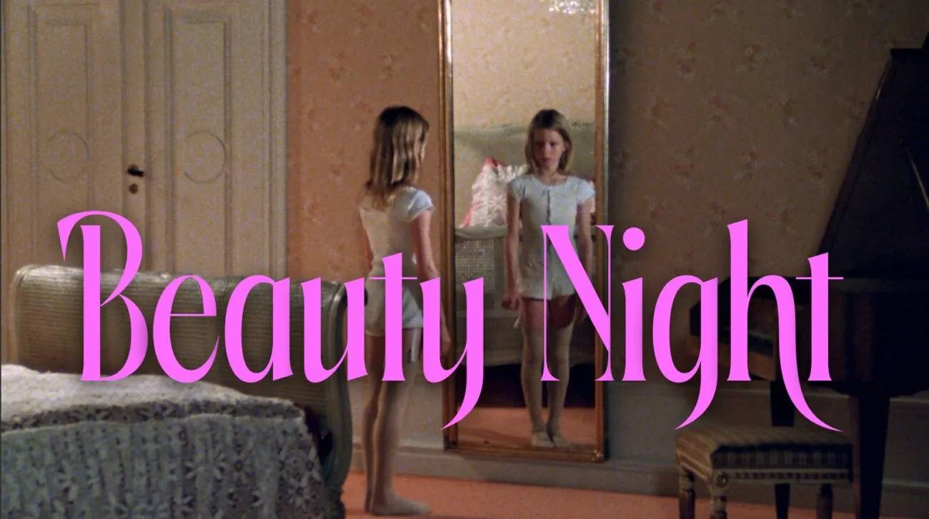 A Young girl looks at herself in a mirror behind the words BEAUTY NIGHT written on screen.