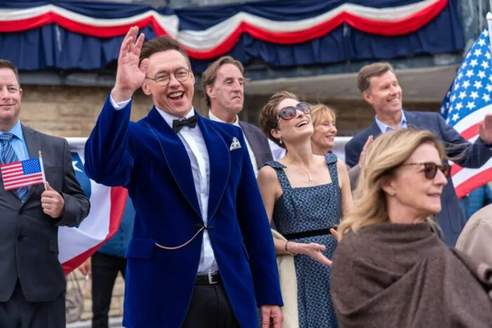 A man in a blue suit is waving in a crowd at a celebratory event