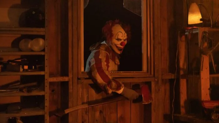 A clown with an axe makes his way through a broken window in CLOWN IN A CORNFIELD