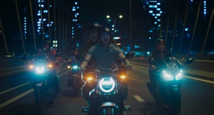 a group of people driving motorcycles at night with the city skyline in the background.