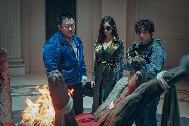 Three people watching a fire burn, one is filming it.
