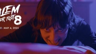A woman is seen at the foot of a bed bowing her head while looking toward the camera with an evil smile in HOUSE OF ASHES