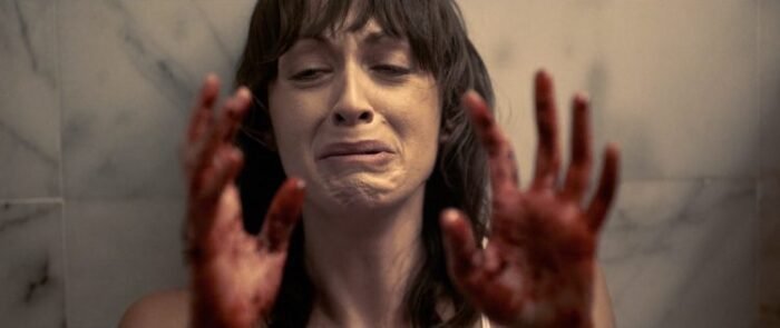 A woman looks at her blood soaked hands in HOUSE OF ASHES