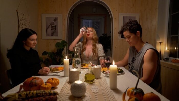 A woman at the head of the table finishes her wine while two other women sit across from each other during dinner in THE REBRAND