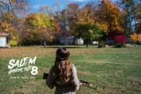 A young girl wearing a crown of ammunition is seen looking at the tree-line perimeter while holding a gun in SO FADES THE LIGHT
